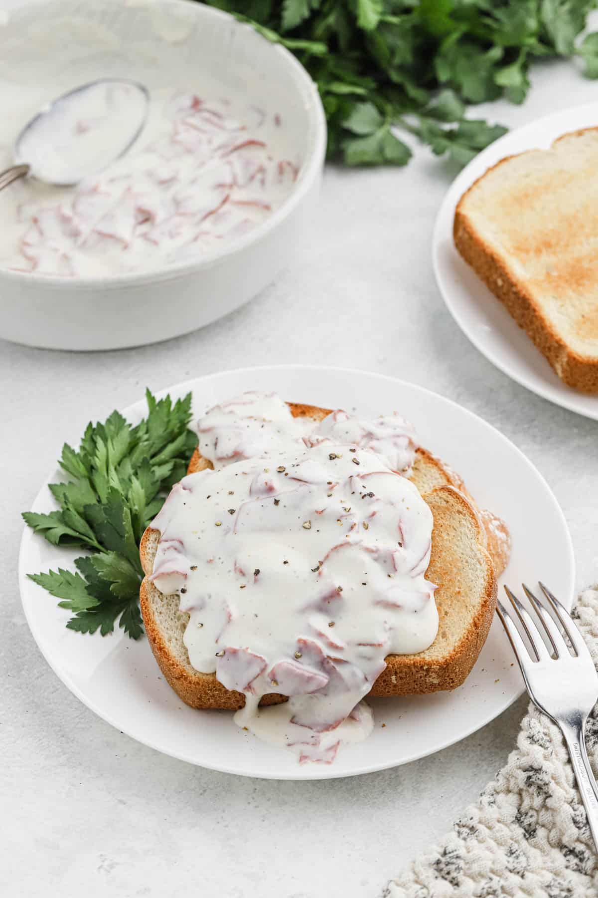 Chipped beef gravy on toast garnished with herbs on a white plate with a metal fork