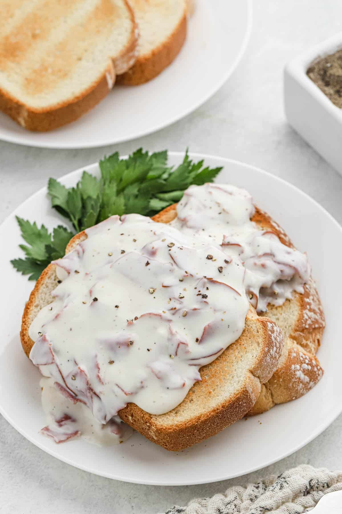 chipped beef gravy on toast garnished with herbs on a white plate