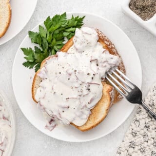 chipped beef gravy on toast garnished with herbs on a white plate with a silver fork