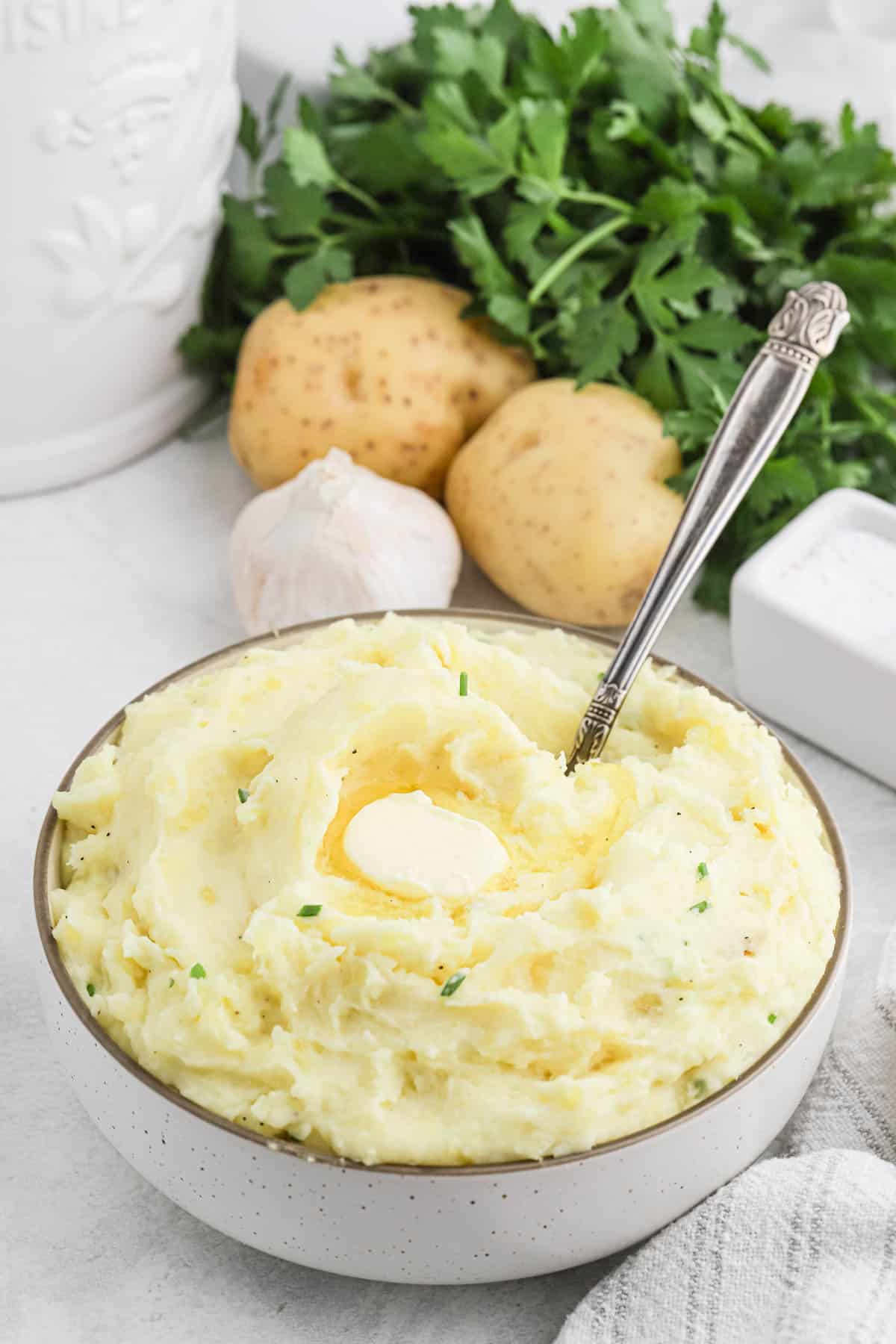 White bowl full of cream Cheese Mashed Potatoes with melted butter and a silver spoon in it
