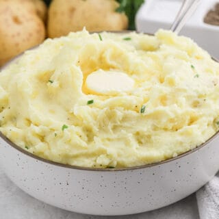Cream Cheese Mashed Potatoes in a white bowl with chives and melted butter