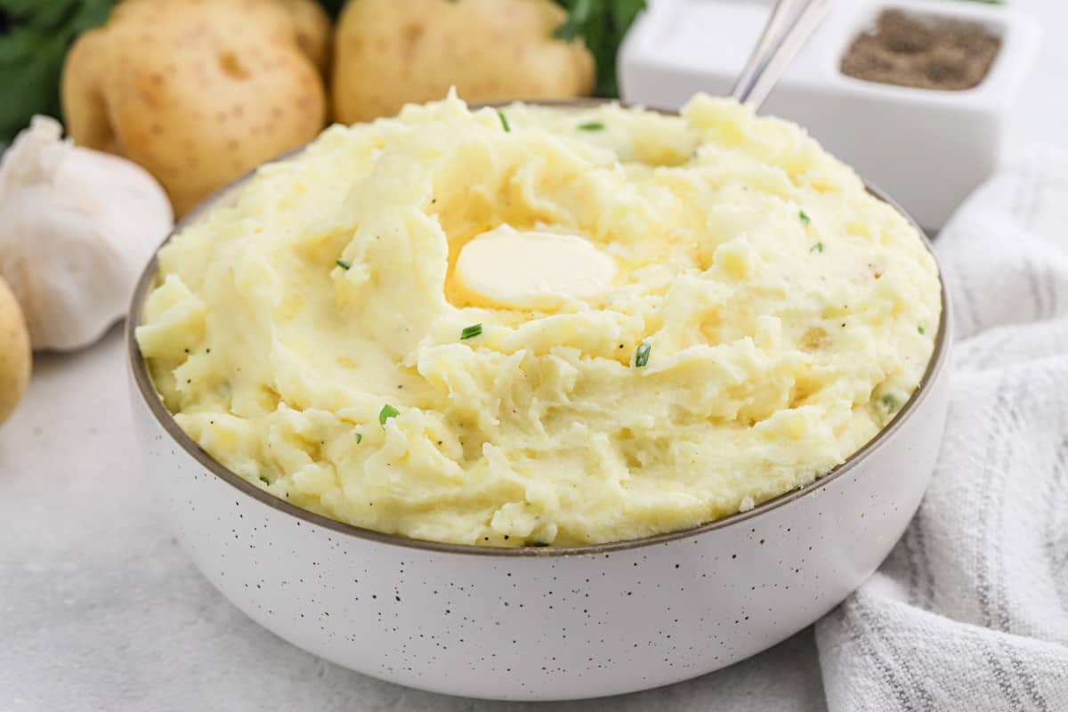 Cream Cheese Mashed Potatoes in a white bowl with chives and melted butter