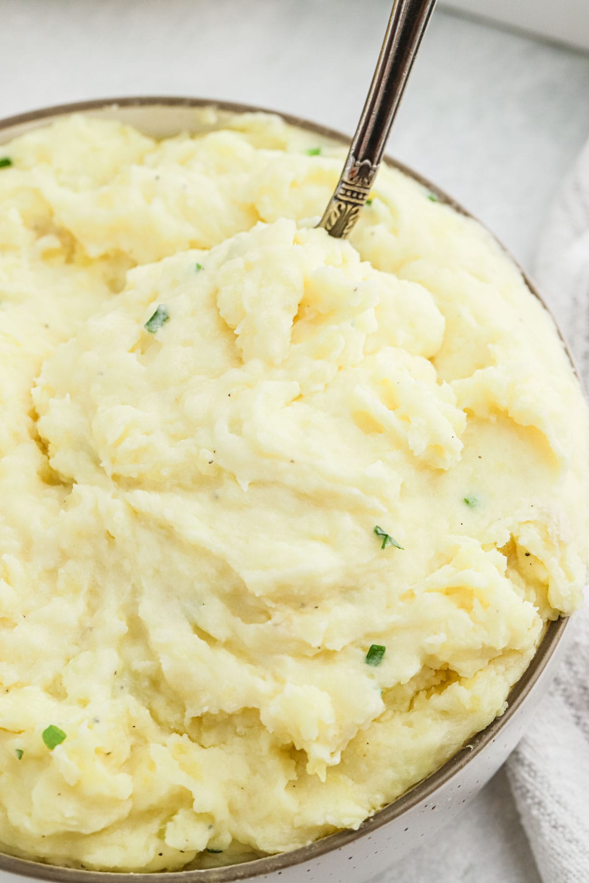 A silver spoon in a bowl of Cream Cheese Mashed Potatoes with chives