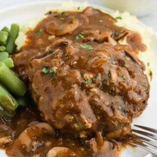 Salisbury steak on a white plate with green beans and mashed potatoes