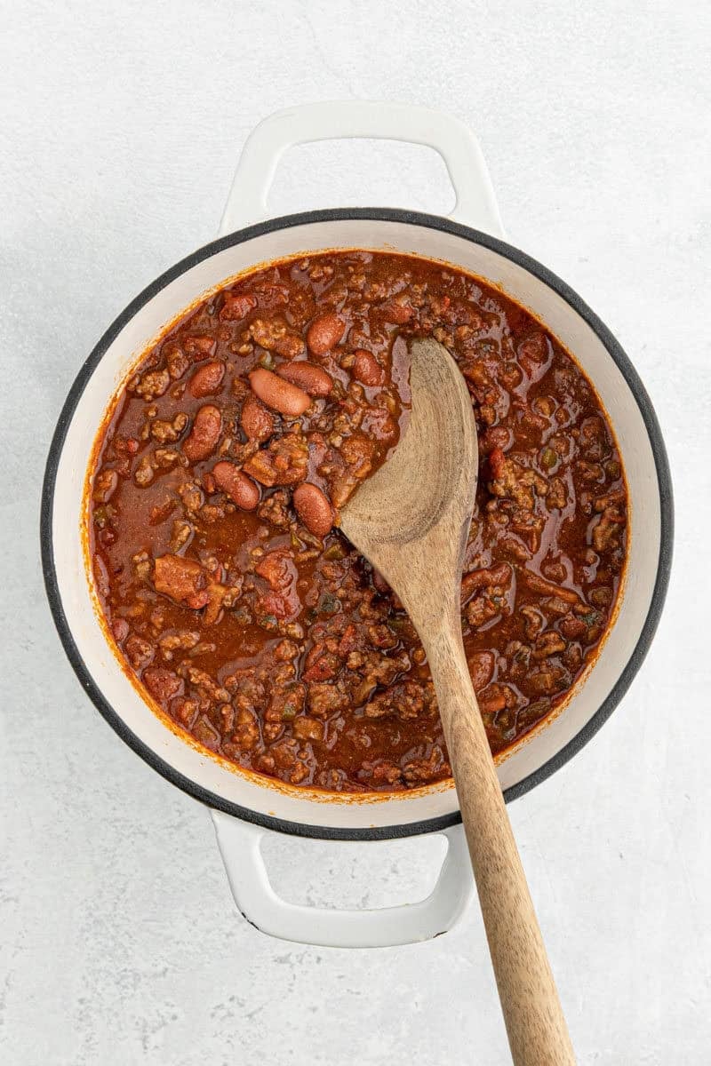 A rich, thick chili with ground beef, beans, and tomatoes, stirred with a wooden spoon