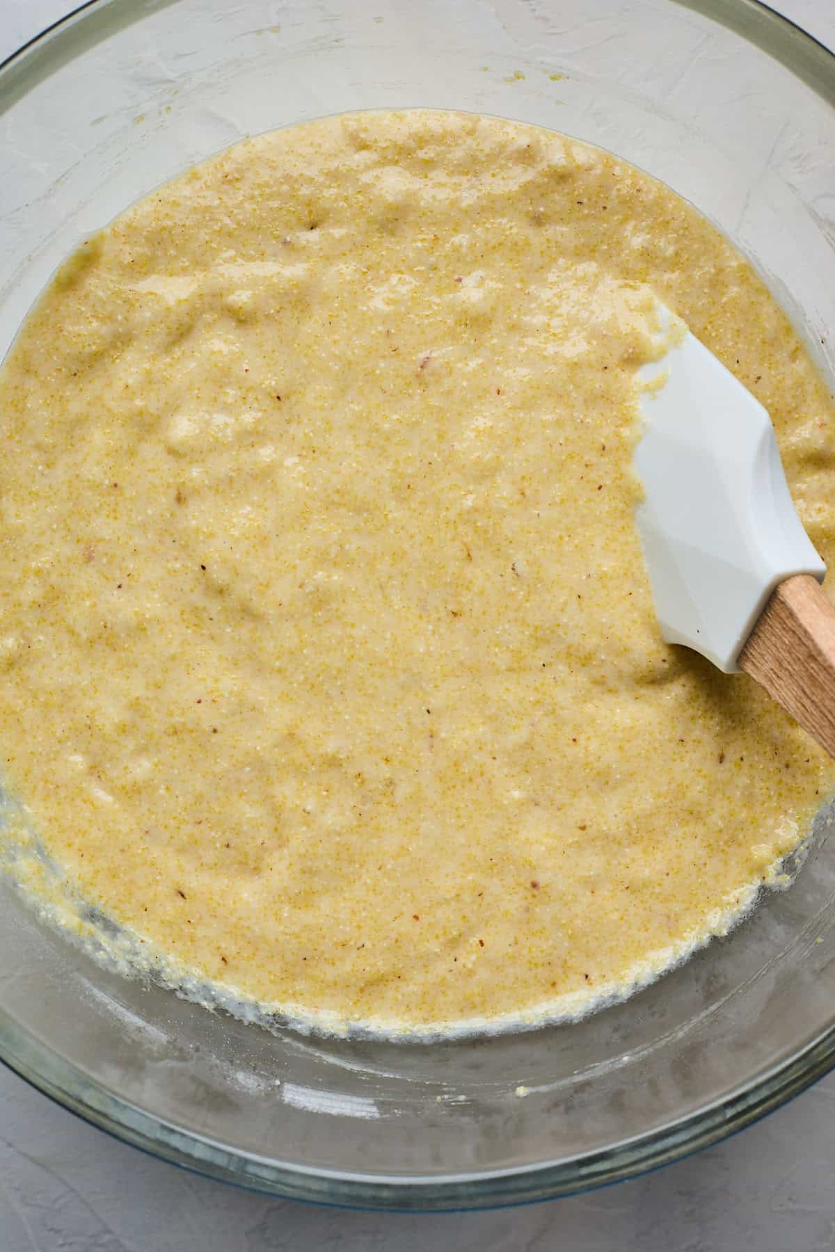 Honey cornbread mixture being folded over with a spatula in a glass bowl