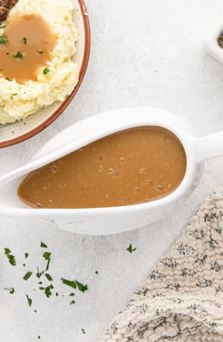 Brown gravy in a white gravy boat next to a plate of salisbury steak and mashed potatoes