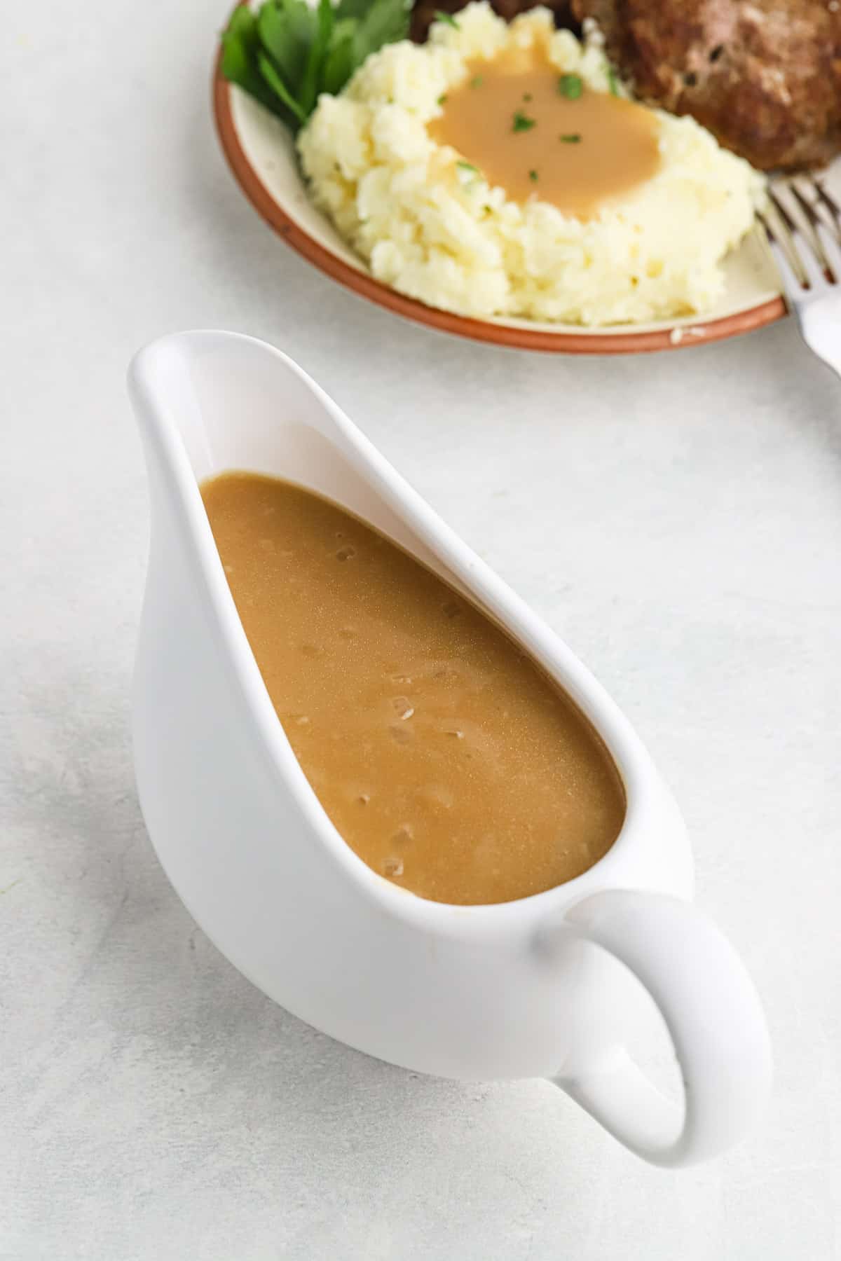 Brown gravy in a white gravy boat with mashed potatoes and salisbury steak in the background