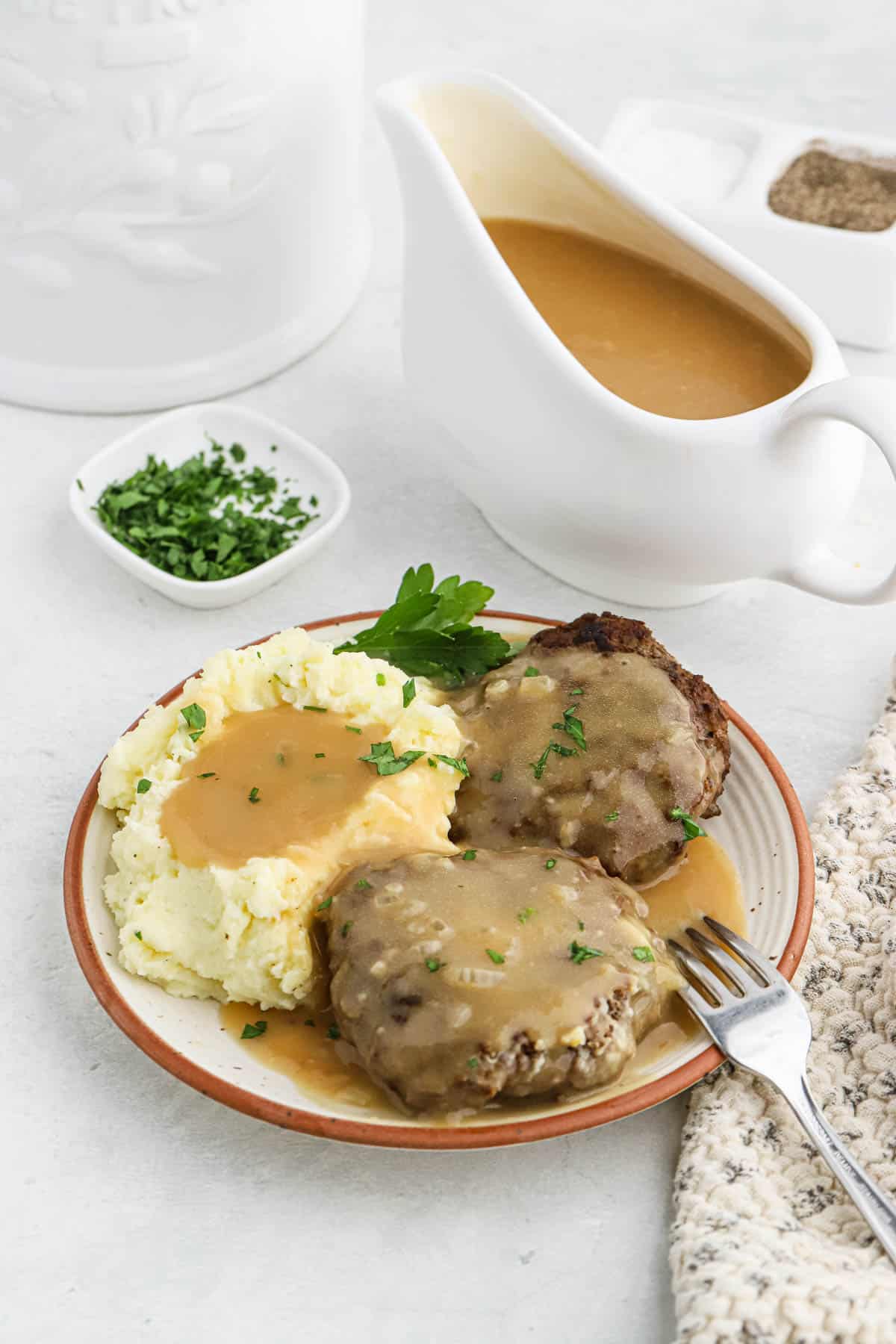A plate of mashed potatoes and salisbury steak with brown gravy on top and a gravy boat next to it