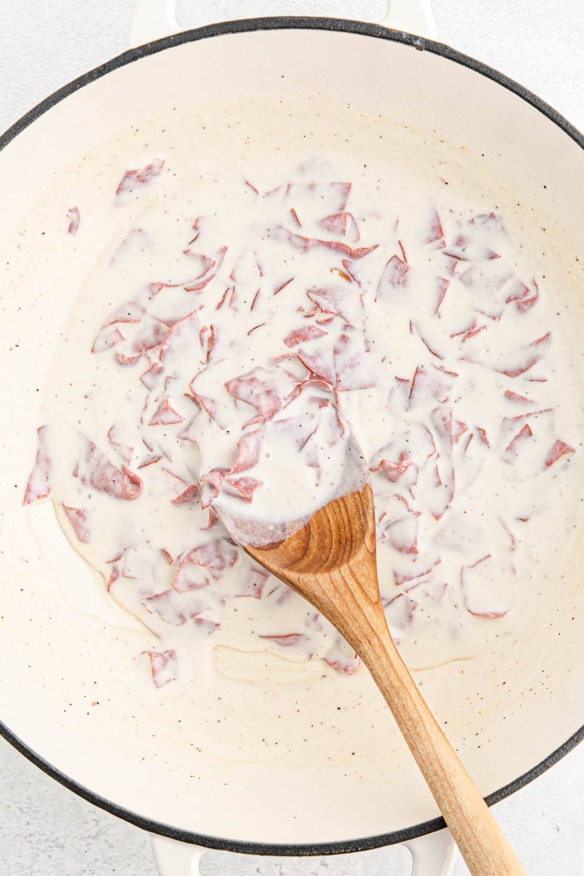 Chipped beef gravy simmering and thickening with a wooden spoon in the pot