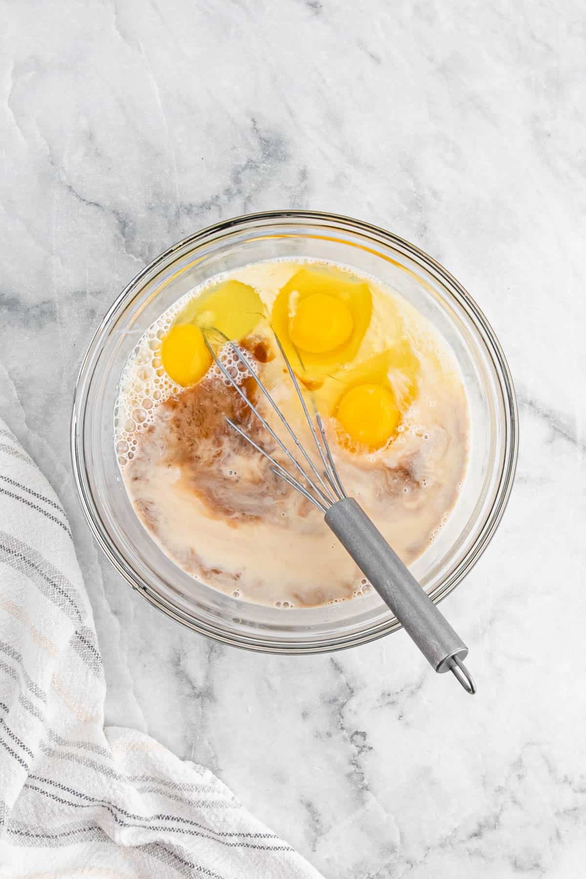 Eggs, evaporated milk, condensed milk, rum, salt, and vanilla extract in a glass bowl with a whisk before mixing