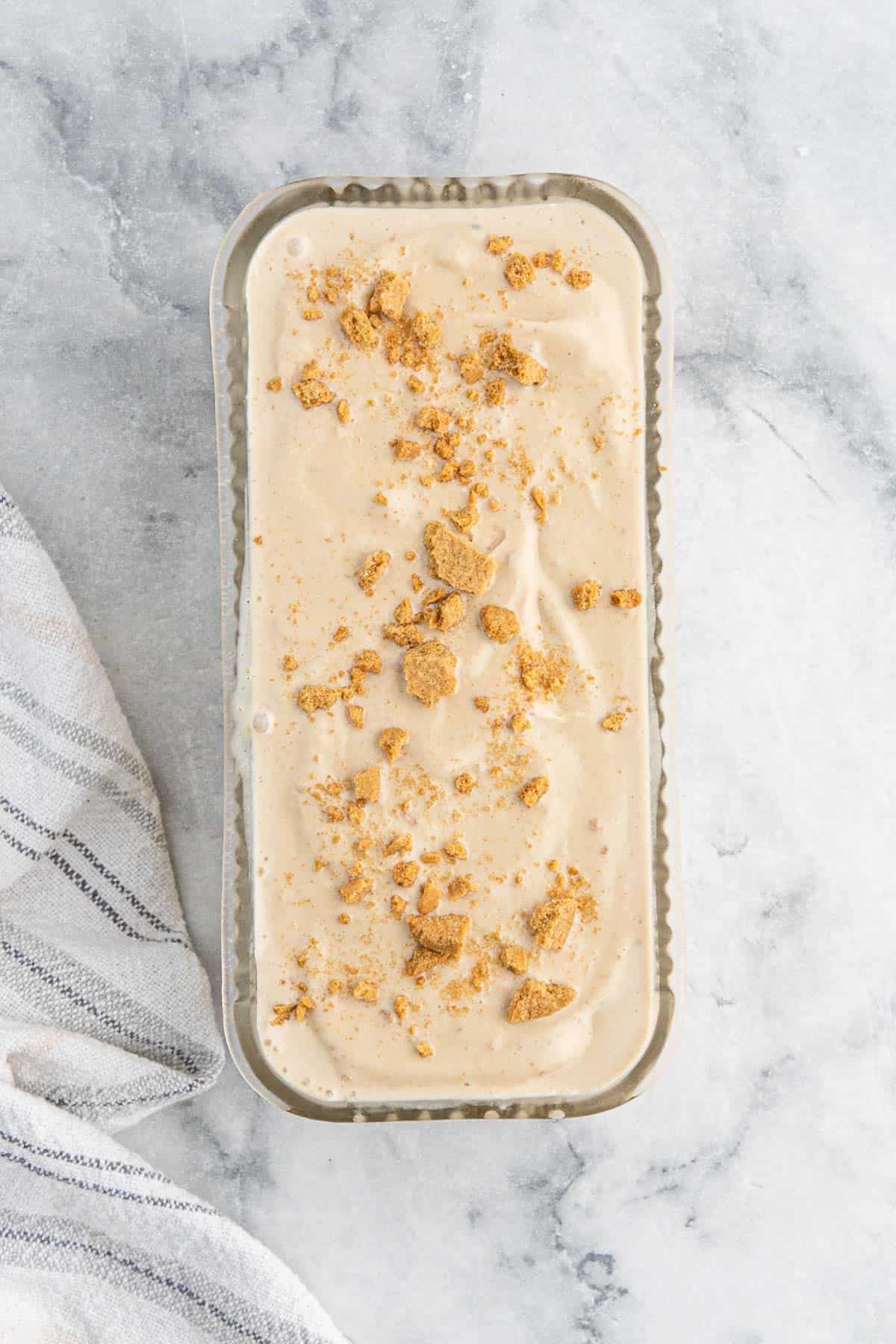 Cookie butter ice cream in a loaf pan topped with crushed gingersnap cookies on a marble countertop