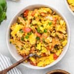 Saltfish and ackee in a white bowl with a spoon in it surrounded by various ingredients