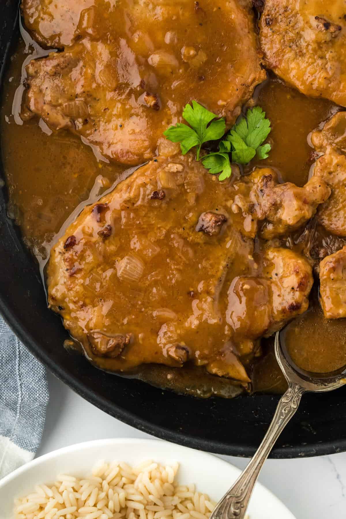 A close up of smothered pork chops recipe in a pan with brown gravy