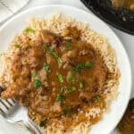 Smothered pork chop recipe over white rice with a silver fork on white plate