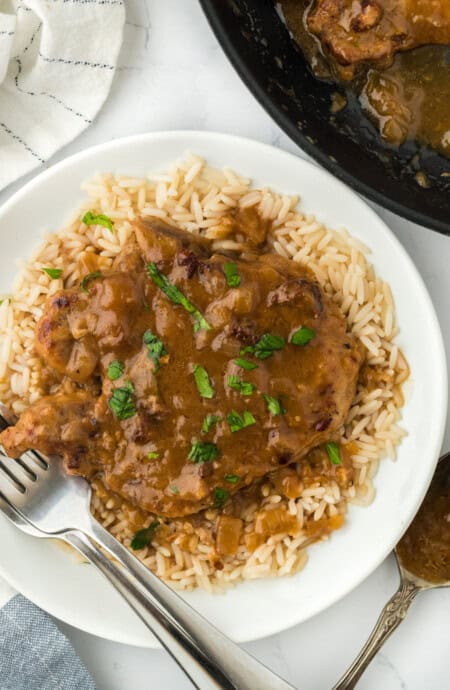 Smothered pork chop recipe over white rice with a silver fork on white plate