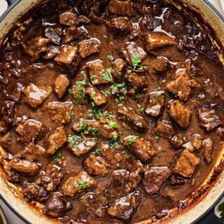 Beef tips with gravy in a large pot topped with herbs