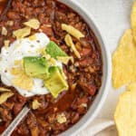 A half a bowl of Southern chili on the table topped with sour cream and avocado.