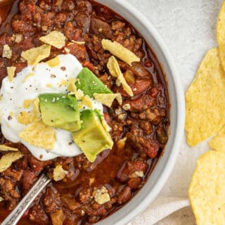A half a bowl of chili on the table topped with sour cream and avocado.