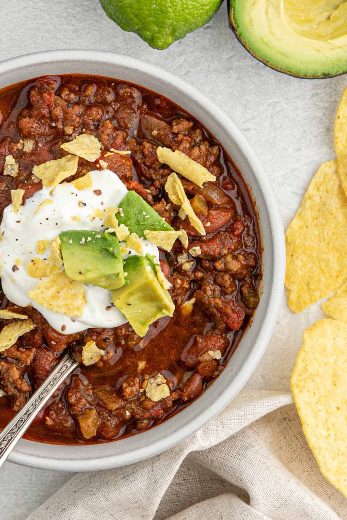 A half a bowl of chili on the table topped with sour cream and avocado.