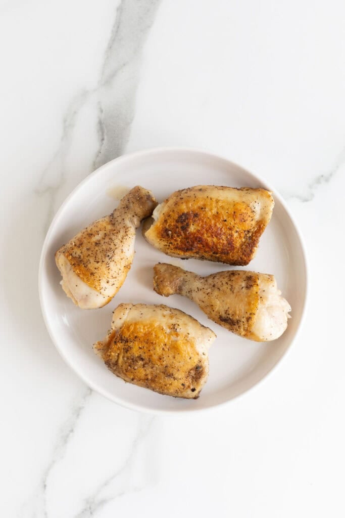 Browned chicken on a white plate after being seared