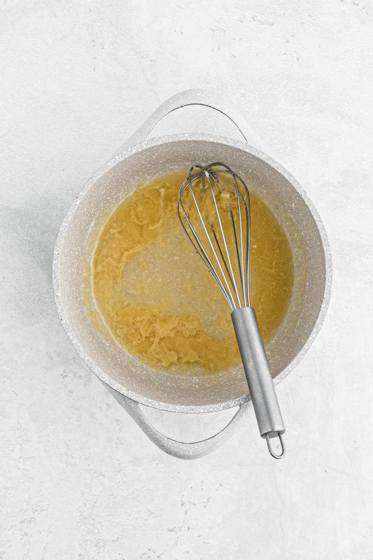 Whisk resting in a saucepan of roux mixture, showing early stages of gravy thickening