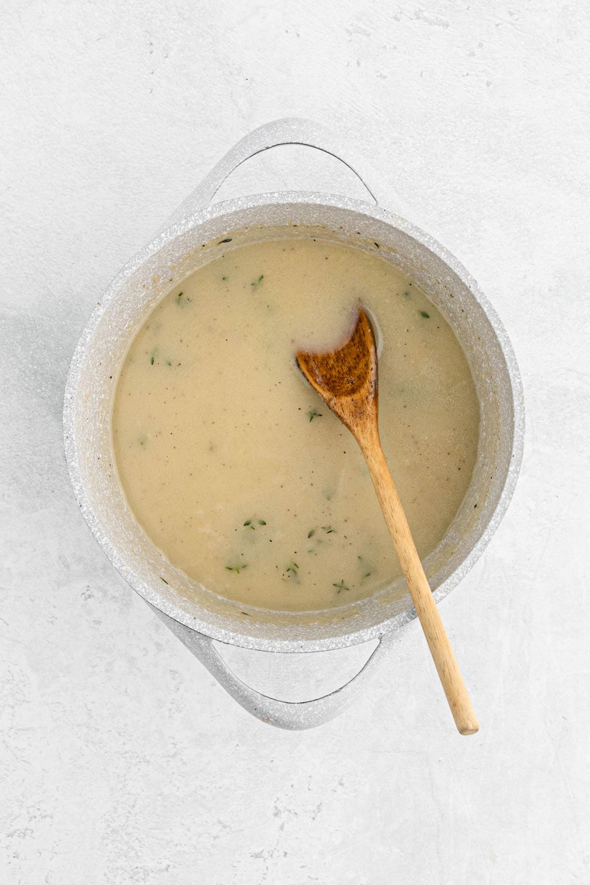 Smooth chicken gravy with herbs in a saucepan, stirred with a wooden spoon