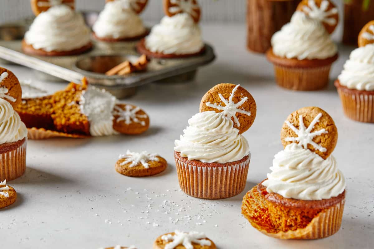 Ginger cupcakes are scattered on a table with a pan in the background and one cut in half and laying on its side.