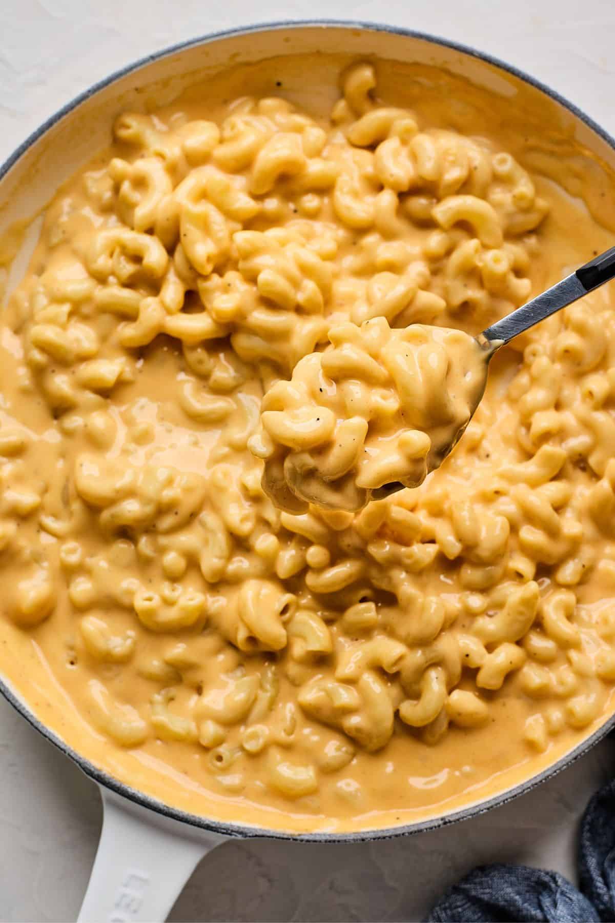 A spoon lifting a scoop of velveeta mac and cheese out of a saucepan after cooking.