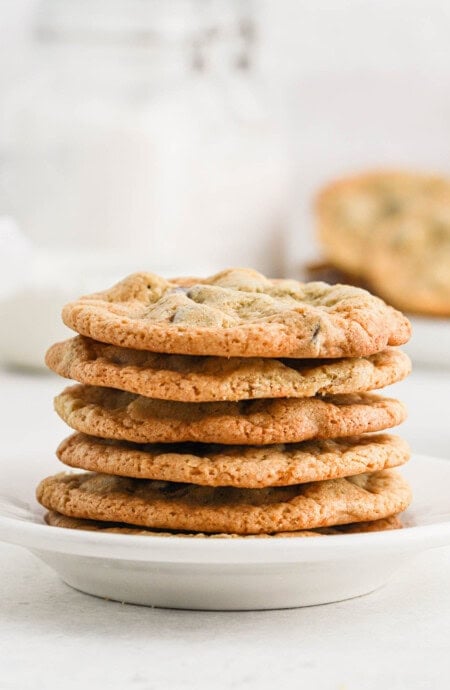 A stack of crispy chocolate chip cookies on a white plate