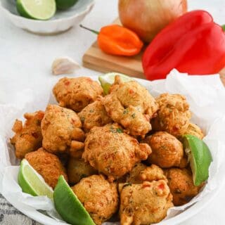 A large white plate of saltfish fritters on white background with peppers and limes in the background