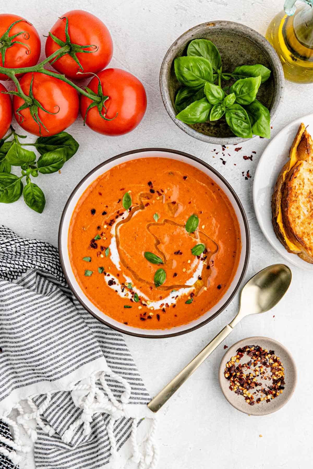 A bowl filled with tomato soup on a white background with tomatoes and parsley in the background