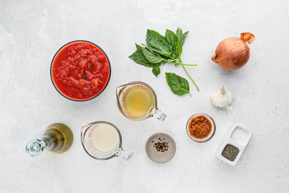 Overhead shot of the ingredients needed to make this simple tomato soup on a white surface