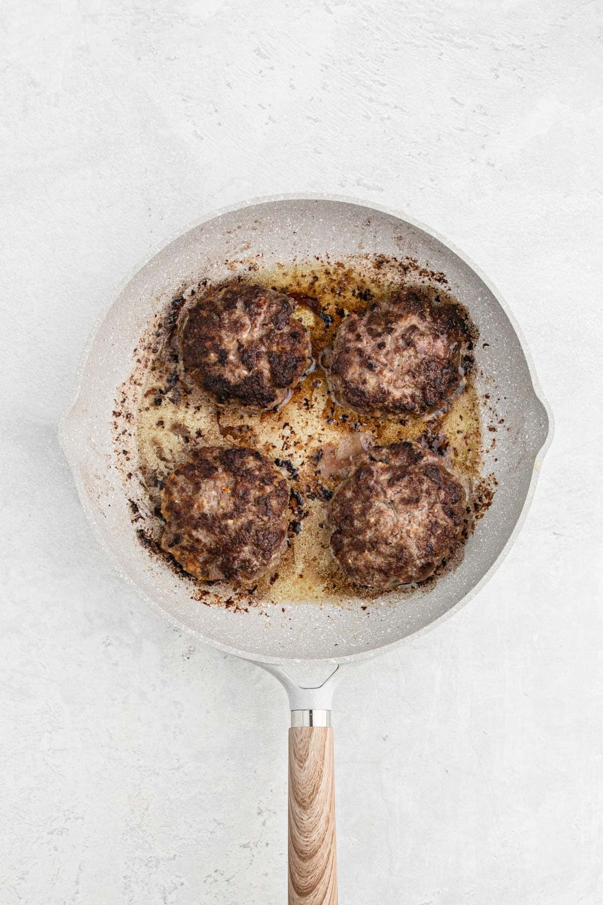 Four Salisbury steak patties searing until browned in a skillet
