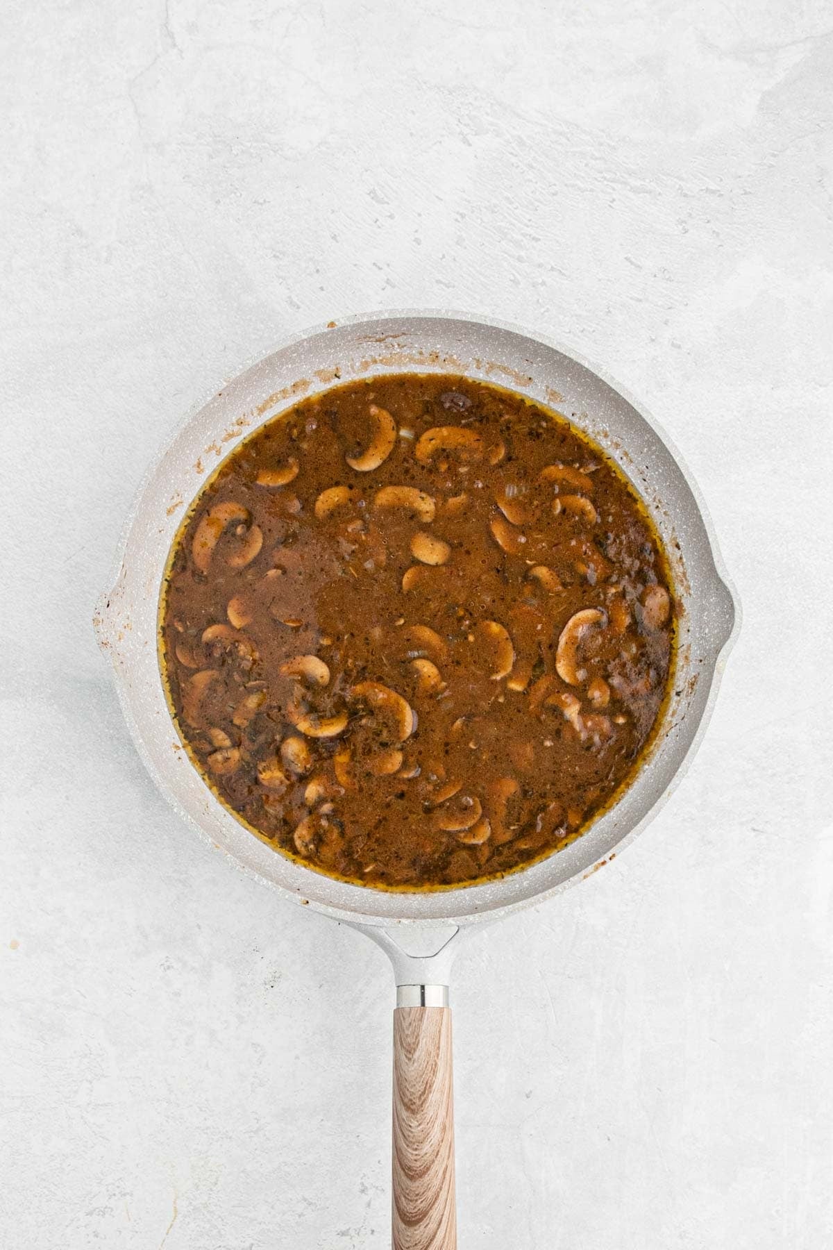 Brown mushroom gravy simmering with sliced mushrooms in a skillet