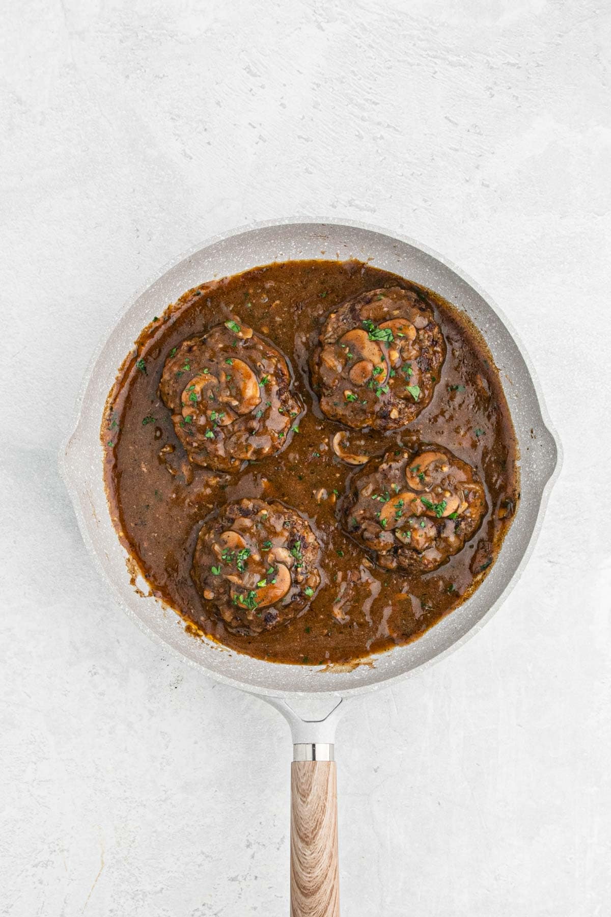 Salisbury steak patties in rich mushroom gravy, topped with chopped parsley in a skillet