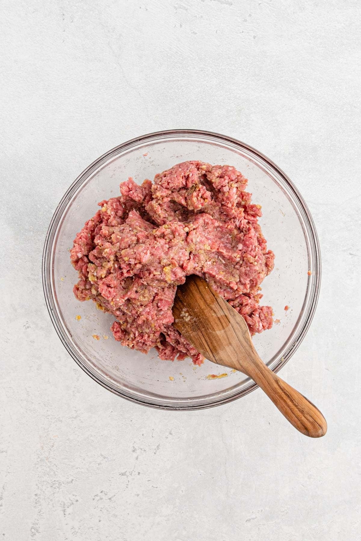 Ground beef mixed with the seasoned breadcrumb mixture in a glass bowl