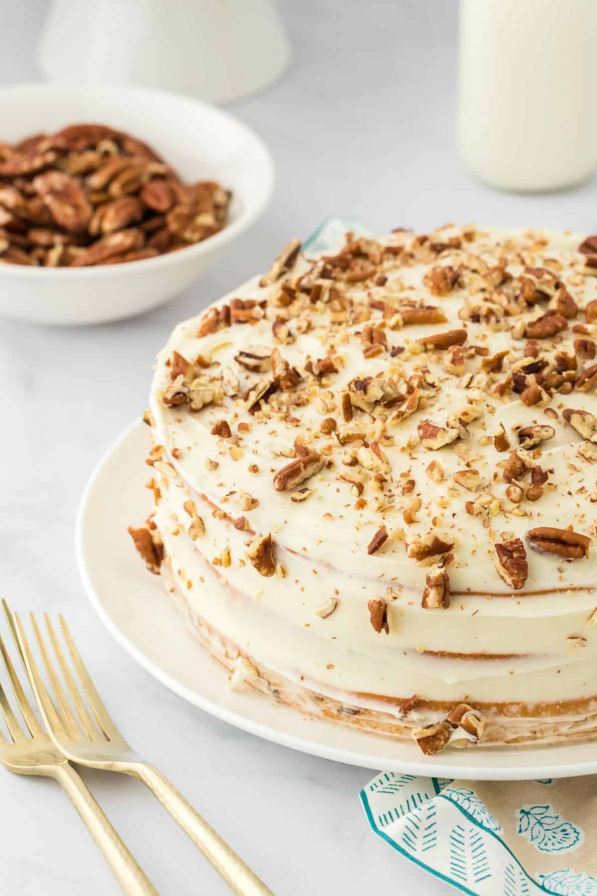 Butter pecan cake on a white cake stand with a plate of pecans in the background