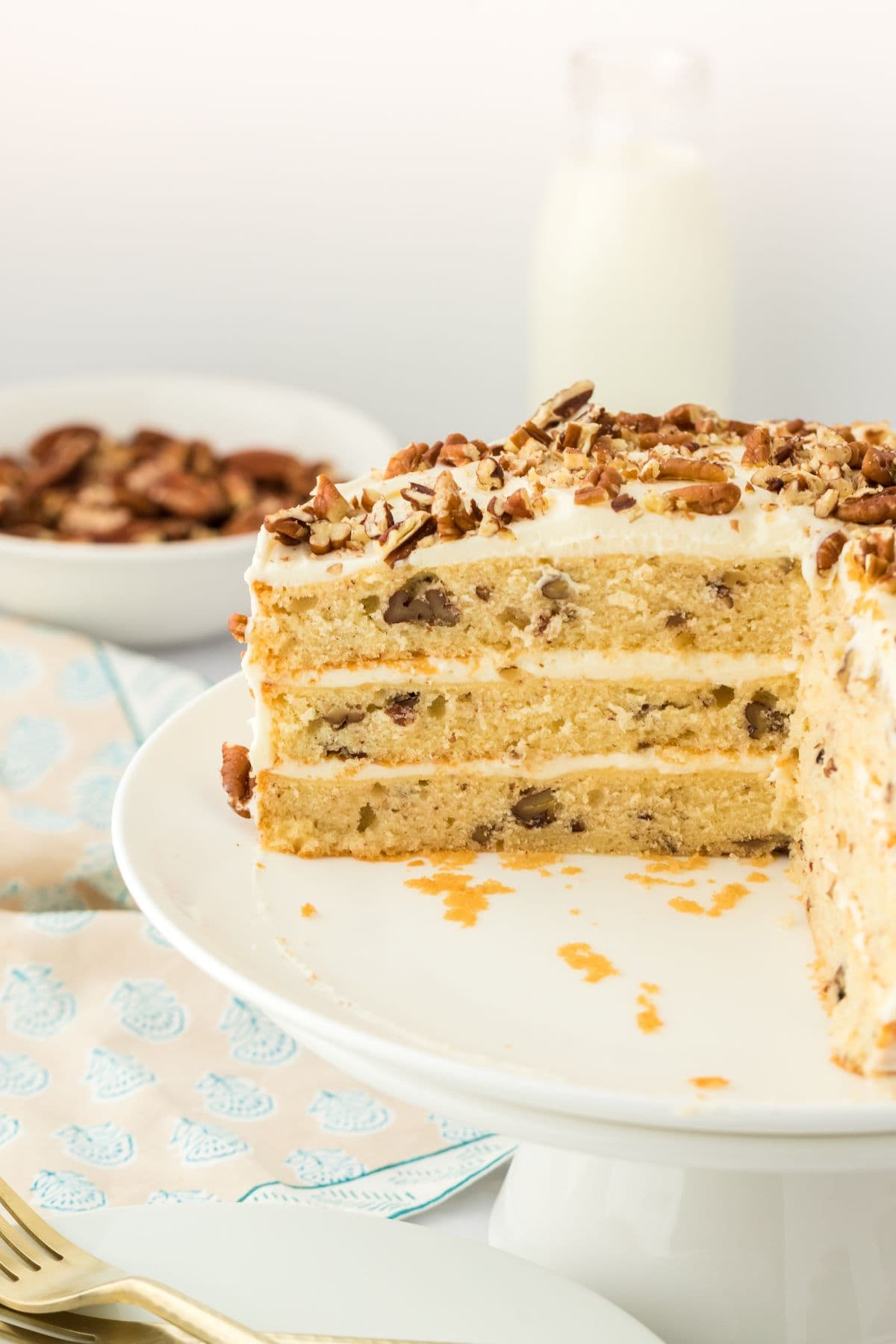 Butter pecan cake with slices missing on a white cake stand