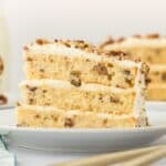 Slice of butter pecan layer cake on a white plate with more cake in the background