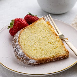 Slice of buttermilk pound cake on a white plate with a fork and a couple of strawberries next to it