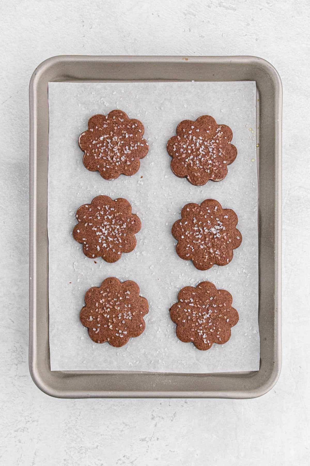 Baked chocolate sugar cookies topped with sugar crystals, cooling on a parchment-lined baking tray