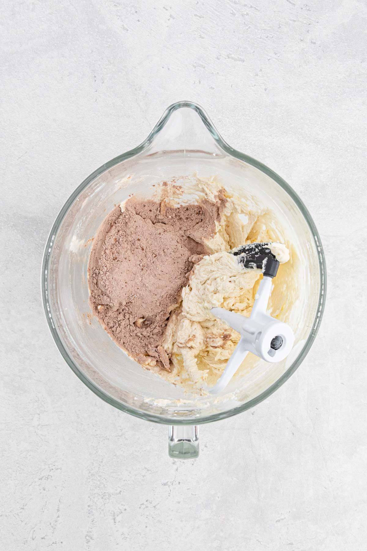 Chocolate dry ingredients being added to the creamed butter mixture in the mixing bowl