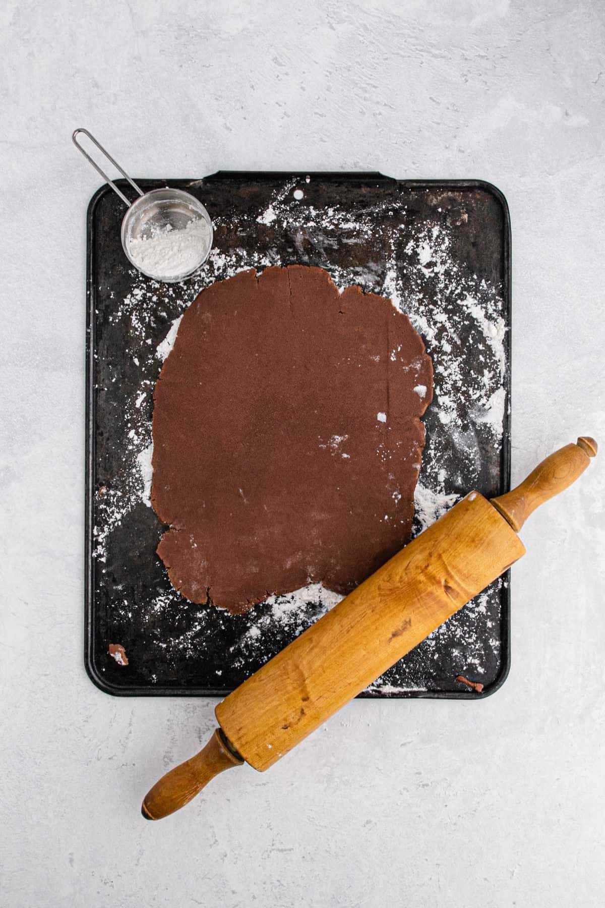 Chocolate cookie dough rolled out on a floured surface with a rolling pin nearby