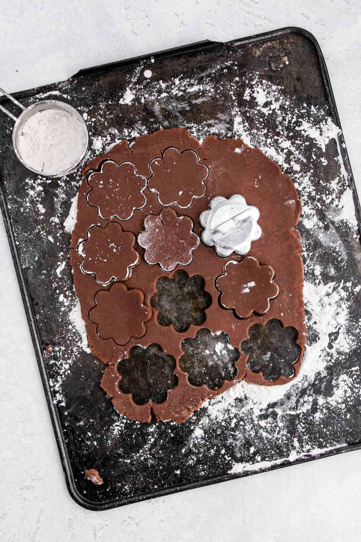 Cookie dough cut into flower shapes with cookie cutters, resting on a floured baking sheet