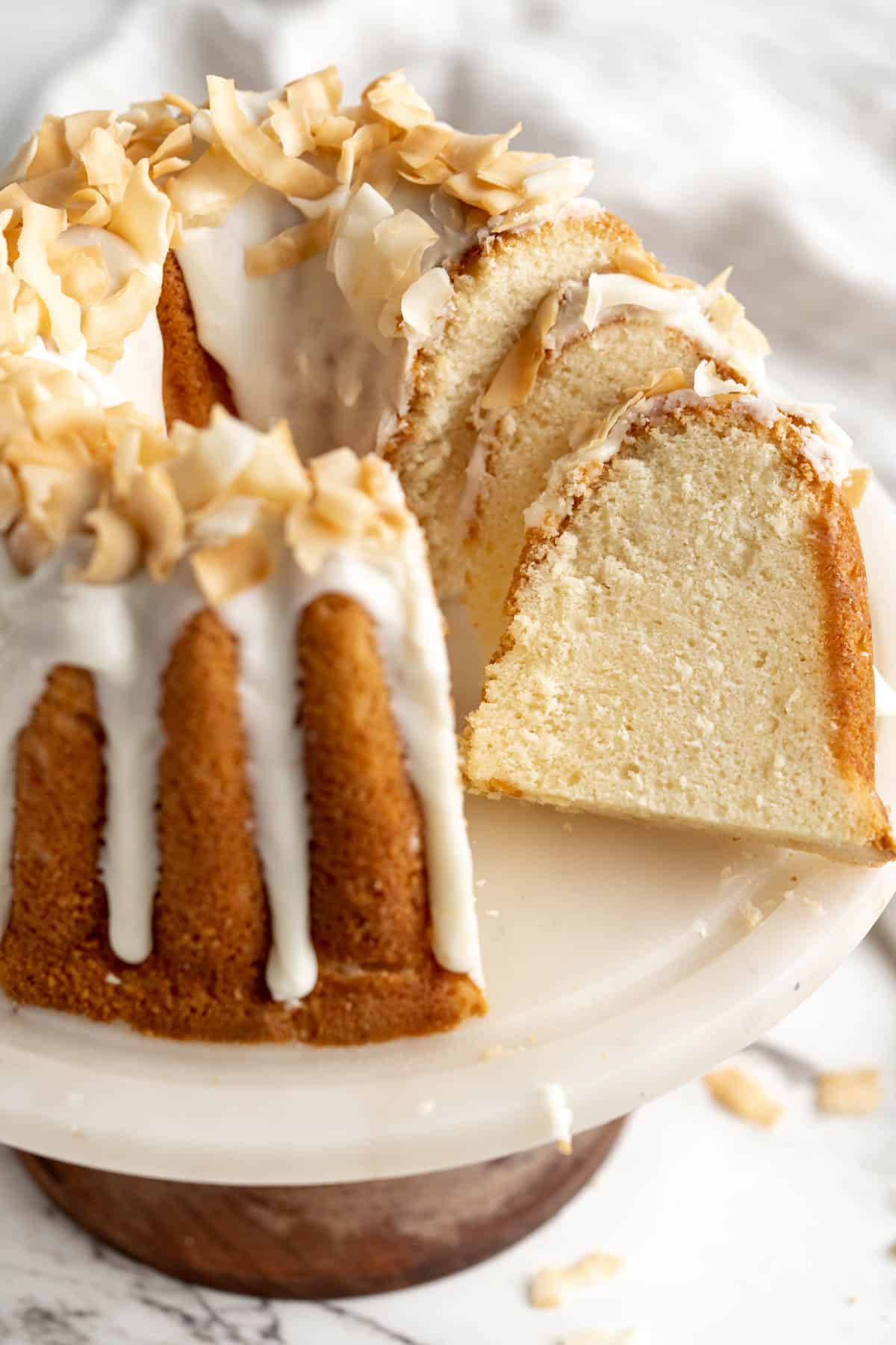 Coconut pound cake with slices cut sitting on a white cake stand