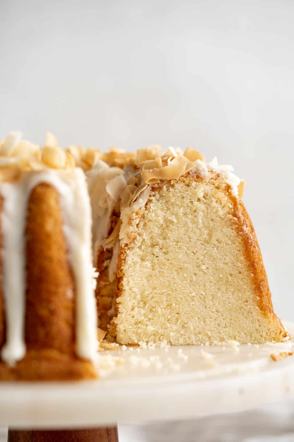 Close up of coconut pound cake with slices missing on a white cake stand