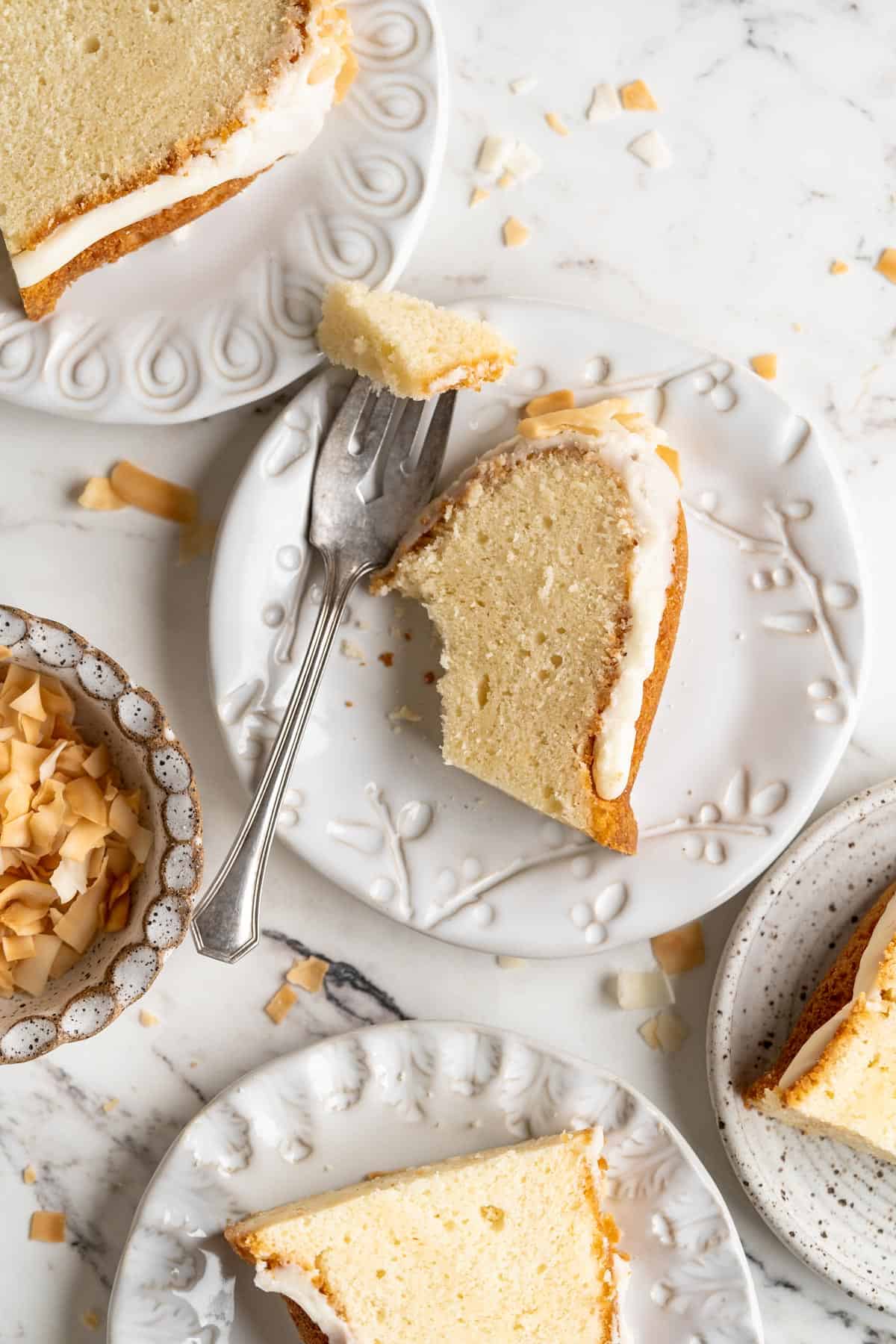 Several slices of coconut pound cake on white plates with one slice partially eaten with a fork next to it