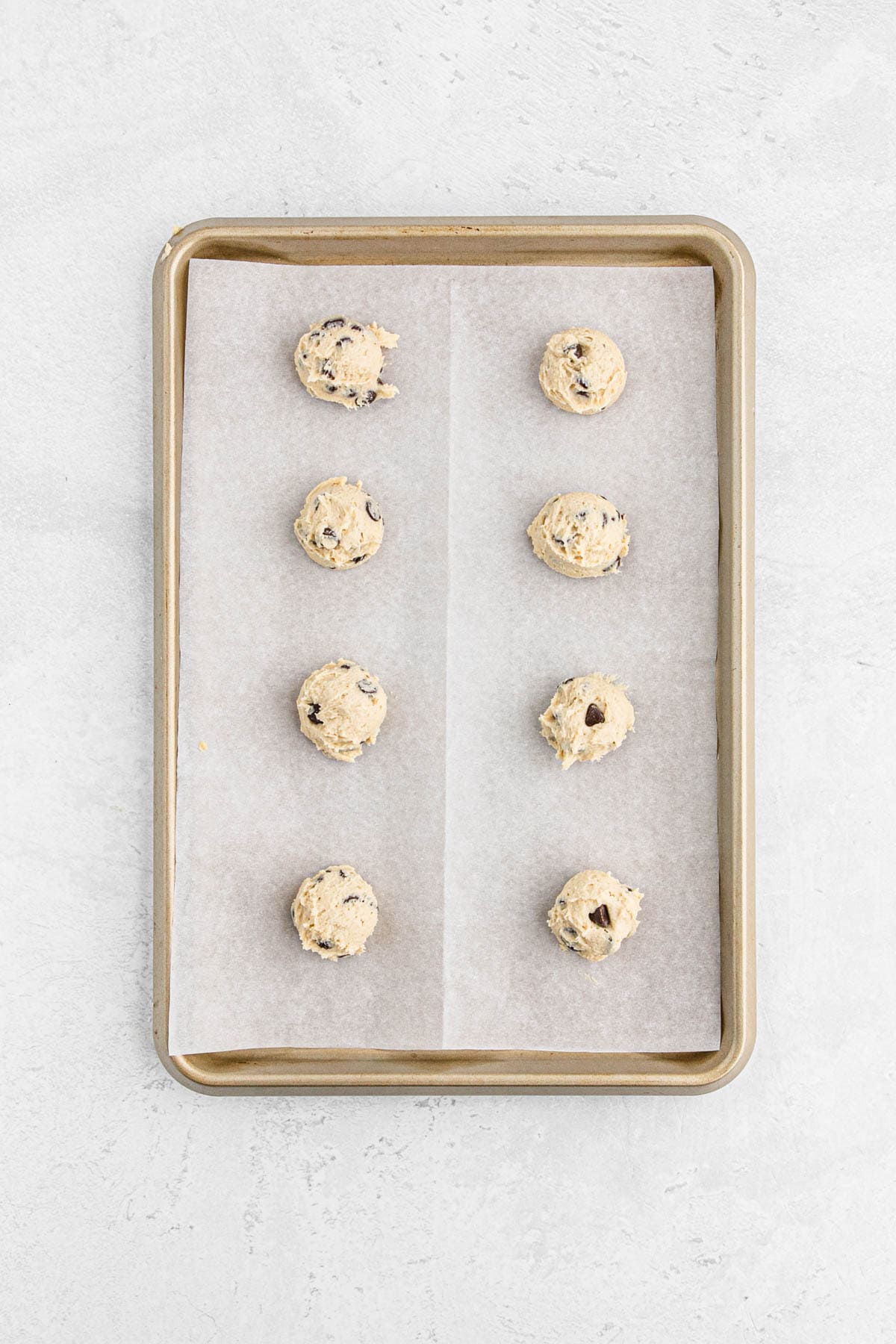 Raw cookie dough balls spaced out on a parchment-lined baking sheet