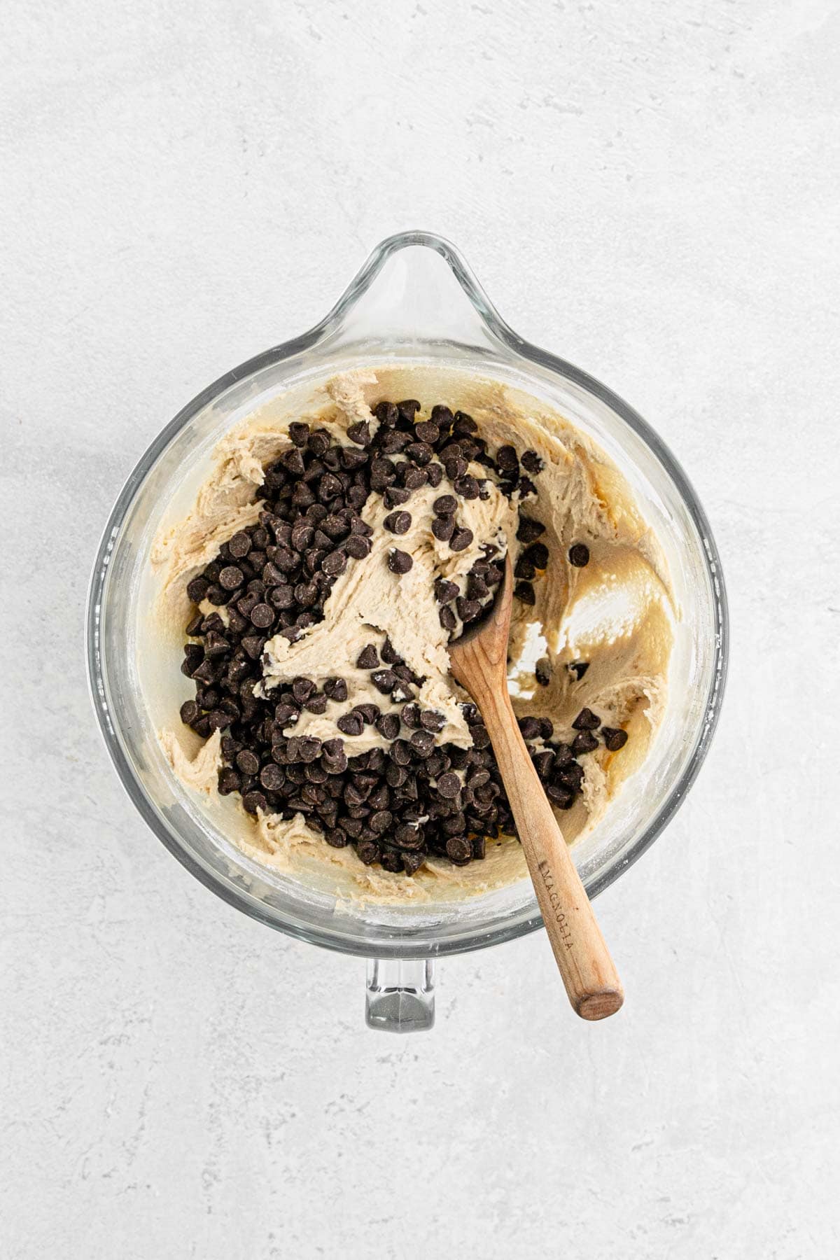 Chocolate chips added to the cookie dough with a wooden spoon in the bowl
